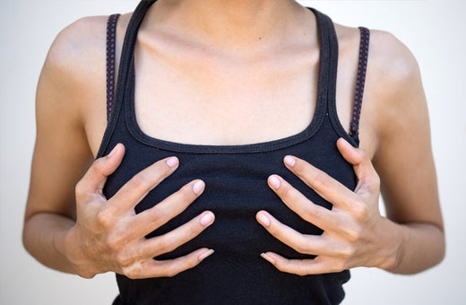 Close-up of a person wearing a black tank top, holding their chest with both hands, often associated with breast discomfort or self-examination.