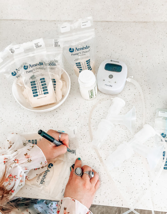 Person writing on a breast milk storage bag, next to a breast pump and bottles on a counter.