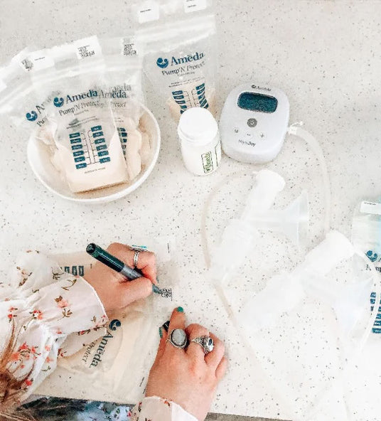 A person writing on breast milk storage bags with a pen, surrounded by breast pump equipment and storage bags on a countertop.
