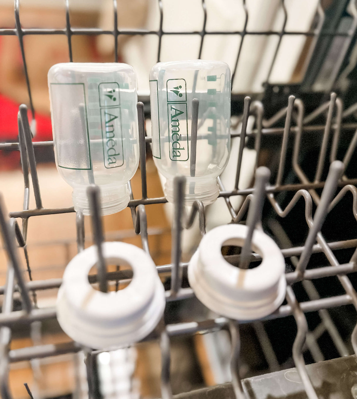 Two Ameda baby bottles and lids placed upside down in a dishwasher rack for cleaning.