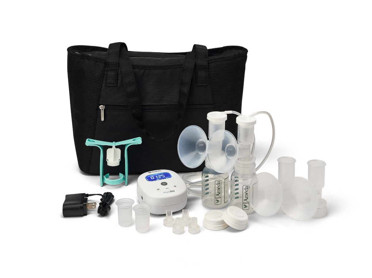 A black tote bag is placed centrally, surrounded by various components of a breast pump kit. The kit includes two clear breast pump flanges, a small white electronic unit with a digital display and buttons, and several collection bottles with lids. There are also small clear lids and connectors, as well as a power adapter with a cord. The items are organized in a way that highlights their functionality for breastfeeding mothers.