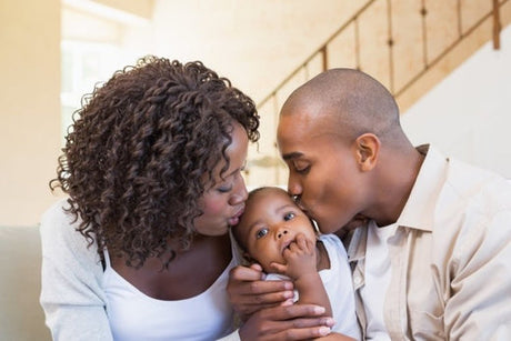 Two parents kissing their baby's head on the couch