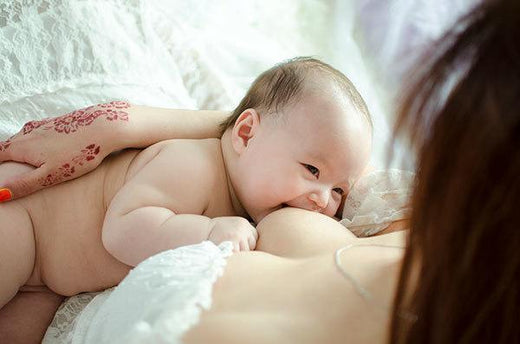 Baby breastfeeding while lying on their mother’s chest, with the mother’s hand gently supporting the baby.