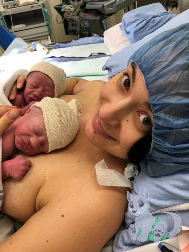 Mother in the hospital bed after delivering the twins on her chest, smiling at the camera.