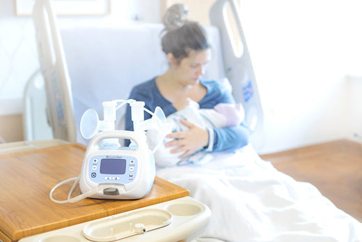 Ameda breast pump on a hospital table with a mother in the background sitting in a hospital bed, holding her baby.
