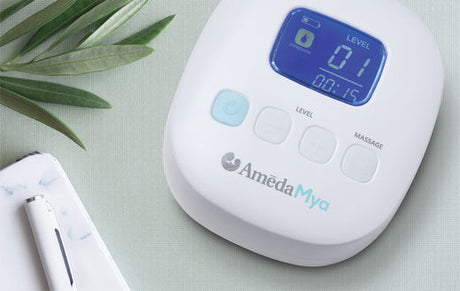 Ameda Mya breast pump device with digital display showing level 1 and timer at 15 seconds, placed on a green surface next to a notebook and pen.