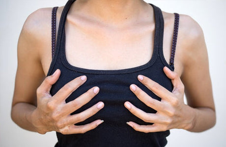 Close-up of a person wearing a black tank top, holding their chest with both hands, often associated with breast discomfort or self-examination.