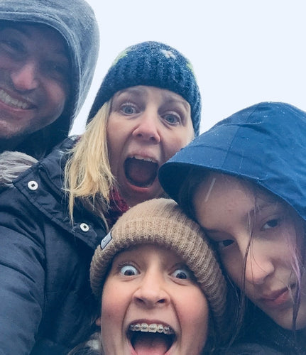 Close-up of a smiling family outdoors in winter clothing, including hats and hoods, making playful faces at the camera.