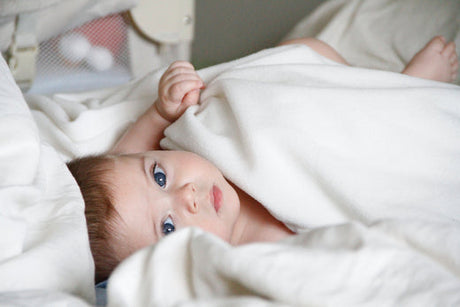 Baby bundled up in sheets, laying on the bed and looking up at the camera
