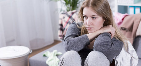 Depressed looking young woman sitting on the couch deep in thought