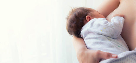 Close-up of a baby breastfeeding, cradled in a parent's arms against a soft, light background.