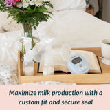 Ameda Mya Joy PLUS breast pump and CustomFit 2-Piece Flanges displayed on a wooden tray — designed for a custom fit and secure seal to maximize milk production
