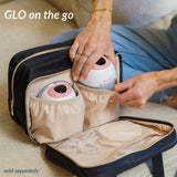 Person placing compact electronic devices into a beige and black travel bag with elastic pockets.