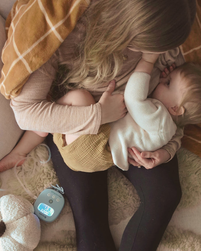 Woman holding a baby on a soft surface with a digital thermometer nearby
